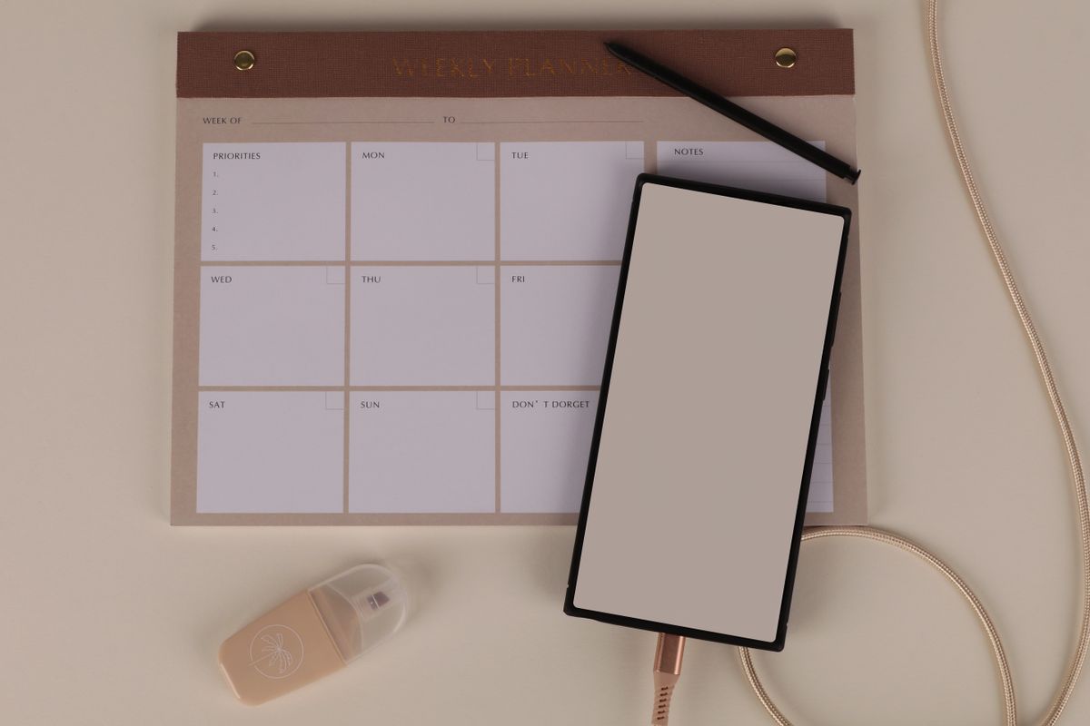 A modern desk setup with a printed weekly planner, phone, and notebook, representing how a week of standing bot reports actually gets reviewed
