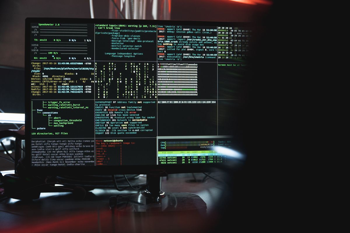 A computer monitor displaying scrolling security console output and code in a dark room